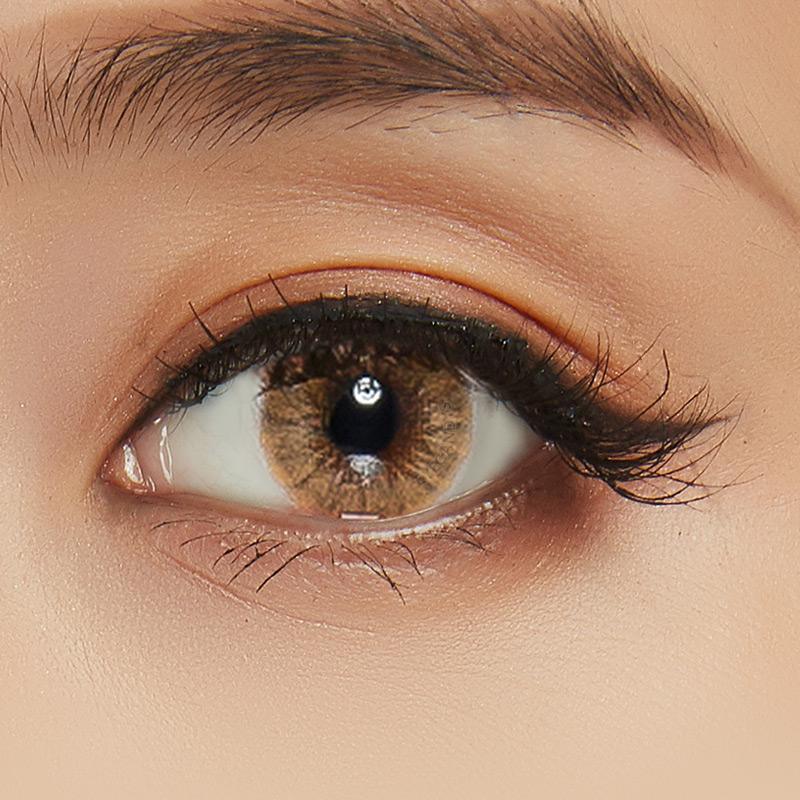 Macro shot of natural brown contact lens with intricate spokes design, modelled on a dark brown eye with natural eye makeup