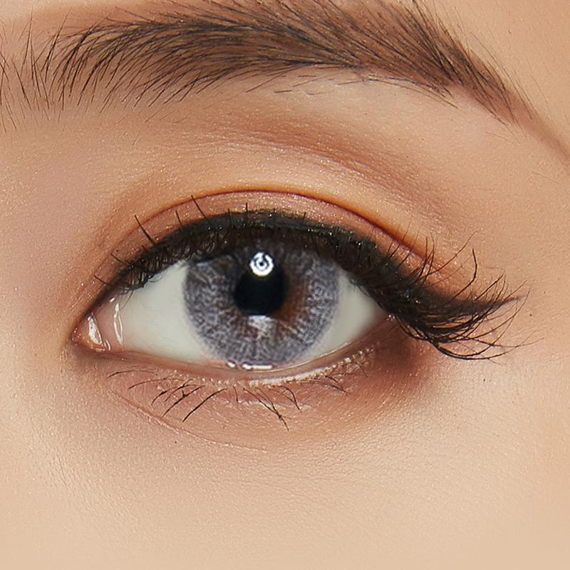 Asian eye wearing Shade Grey contact lenses on top of a dark iris, with natural brown eyeshadow and wispy eyelashes